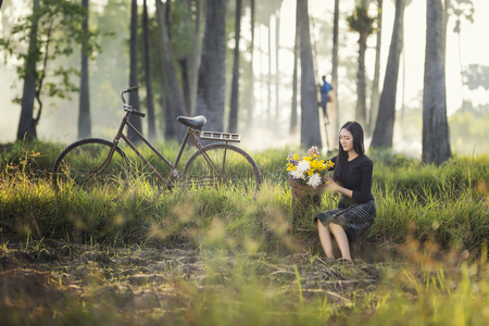 Beautiful Asian woman in local traditional dress with old bicycle and flower basket on the green summer field.の写真素材