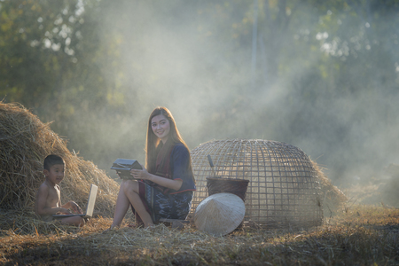 Asian beautiful girl wearing thai traditional dress,lying with brother and listen radio on the straw.の写真素材