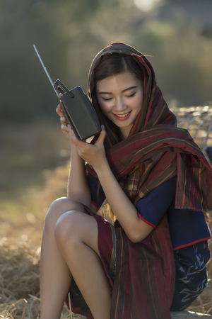 Asian beautiful girl wearing thai traditional dress,lying and listen radio on the straw.の写真素材