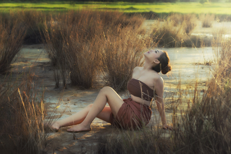 Thai Beautiful woman wearing typical tradition sitting in field alone in eveningの写真素材