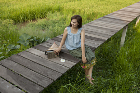 A peasant girl listening to the radio on a wooden bridge in a field,countryside Thailandの写真素材