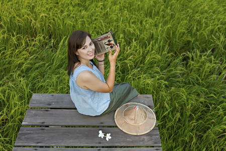 A peasant girl listening to the radio on a wooden bridge in a field,countryside Thailandの写真素材