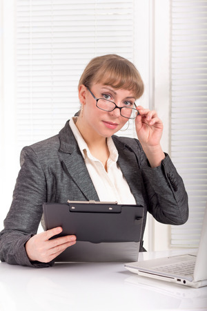 Business woman with glasses dressed in a formal suit sitting at her deskの写真素材
