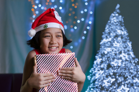 Happy Child Girl in Santa Hat Hold a Gift Box with Christmas Tree.の写真素材