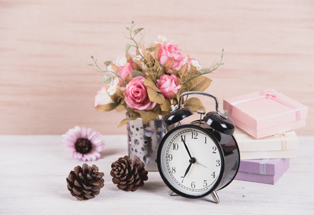 still life interior decoration pink rose flower in a vase with clock and gift box, pine cones on...