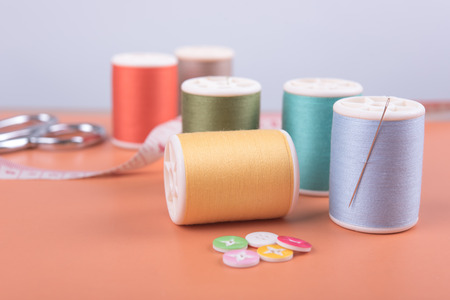 closeup needles, thread spool, scissors, button on wooden background.