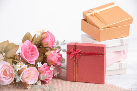 Picture of red gift box with red ribbon with pink rose flower and gift card on wood background....