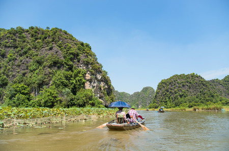 Tourists asia traveling in boat along nature the river and mountain. at Tam Coc portion, Ninh Binh Province, Vietnam. Rower using her feet to propel oars. landscape river and mountainのeditorial素材