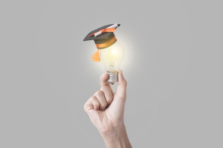 student hand holding light bulb with graduation hat on gray background. concept education of new ideas with innovation and creativity.の写真素材