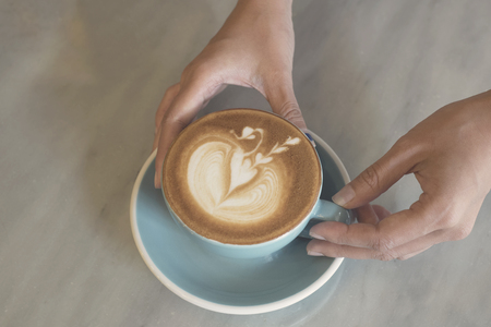 closeup hand holding coffee latte art cup on table.の写真素材
