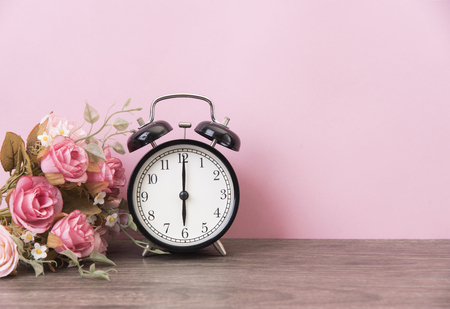 alarm clock and rose on wood table with pink background and copy space for product display montage.の写真素材