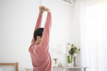 man sitting near the window and stretching hand on bed after waking up in morning time.の写真素材