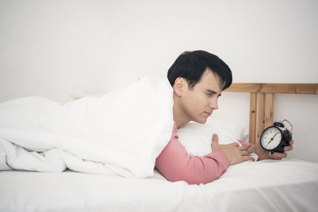 Man wake up doing turn off alarm clock in the morning. He tired and lazy do work.の写真素材