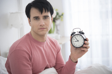 Man wake up doing turn off alarm clock in the morning. He tired and lazy do work.