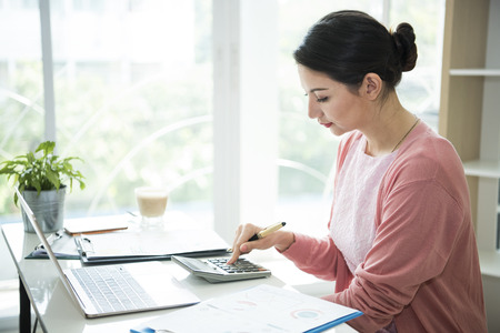 Businesswomen using calculator with analyzing financial figures on a graphs in office.の写真素材