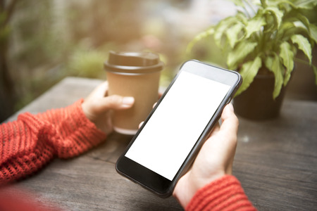 A woman using mobile phone with blank white screen and holding a coffee cup. Social media technology...
