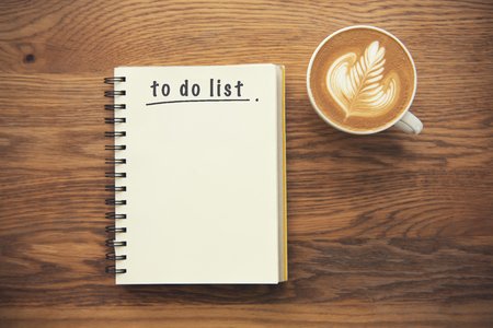 Coffee cup and notebook with to do list on rustic desk from above, planner and checklist concept.の写真素材