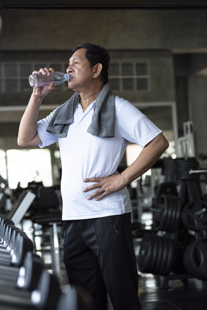 asian senior man thirsty drinking water after exercise in fitness gym. elderly healthy lifestyle.の写真素材