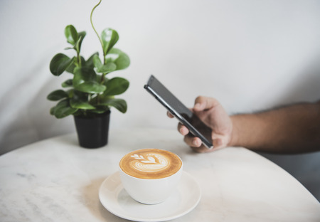 Hand using smart phone on social media with coffee latte cup in coffee shop, life style in everyday.