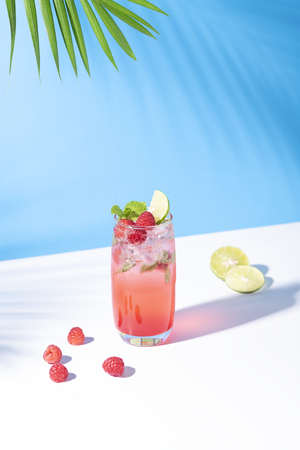 iced red raspberry punch cocktail with lime in glass on blue background. summer drink.の写真素材