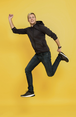 portrait of an excited man jumping while celebrating success over yellow background.の写真素材
