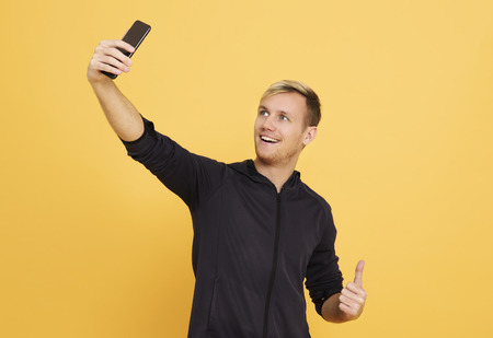 happy man taking selfie on black smartphone over yellow background.