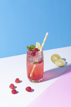 iced red raspberry punch cocktail with lime in glass on color background. summer drink.の写真素材