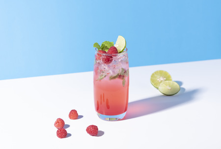 iced red raspberry punch cocktail with lime in glass on color background. summer drink.の写真素材