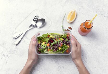 Hand holding fresh healthy diet lunch box with vegetable salad on table background.の写真素材