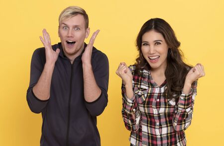 Portrait of happy people man and woman excited smiling while standing together isolated over yellow...
