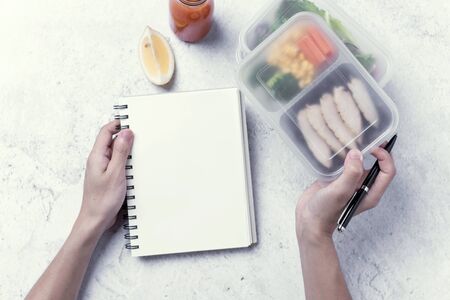 hands holding healthy lunch box and blank notebook for your text message or design, order food concept.の写真素材