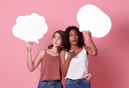 Portrait of two excited young woman holding blank speech bubble and make a face thinking on pink  background.の写真素材