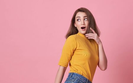 Excited beautiful woman with mouth open and looking at copy space  wearing casual yellow t-shirt isolated on pink background.の写真素材