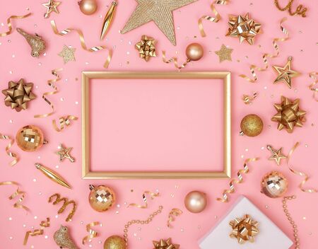 Christmas composition frame with decorations and gift box with golden bows and star confetti on pink pastel background. winter, new year concept. Flat lay, top view, copy space.の写真素材