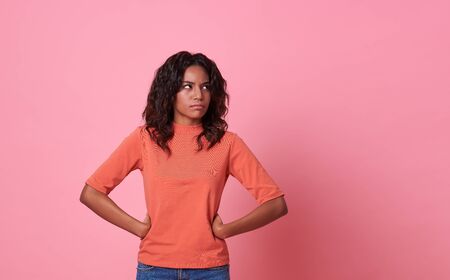 Portrait of an upset unsatisfied woman standing and looking away isolated over pink background.