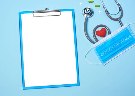 medical equipment mockup clipboard, stethoscope with red heart and drug, surgical mask on blue copy space background.の写真素材