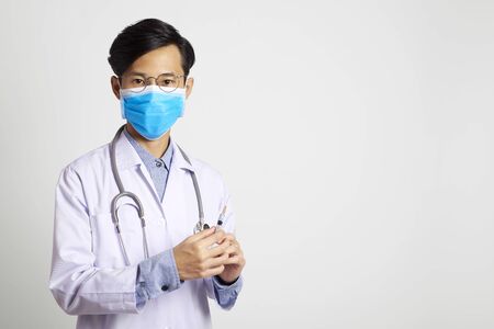 attractive asia man doctor wearing surgical mask and hand holding vaccine syringe standing in gray wall background. Concept Preventive measures against corona virus.の写真素材