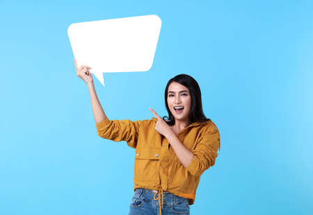 Smiling happy asian woman holding blank speech bubble and with empty space for text on blue...