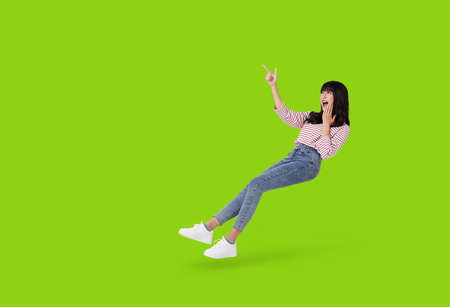 Young beautiful smiling and surprise asian girl floating in mid air with hand pointing up to copy...