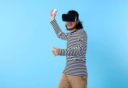 Excited Asian man wearing 3d glasses playing video game on blue background.