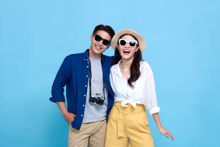 Happy playful Asian couple tourist dressed in summer clothes to travel on holidays isolated on blue background.の写真素材
