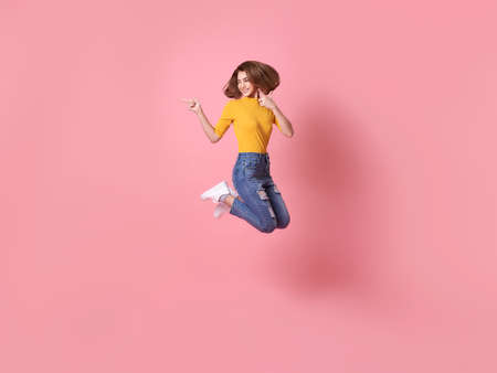 cheerful positive girl jumping in the air with raised hand pointing to copy space isolated on pink background.の写真素材