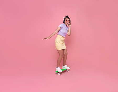 Young asian teenage girl playing on skateboard with wearing wireless headphones listening to music...