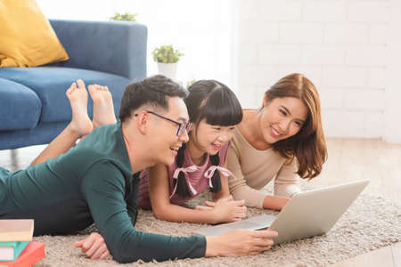 Happy Asian family using computer laptop together on sofa at home living room.の写真素材