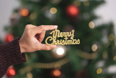 Woman hand holding merry christmas text for decorating a Christmas tree in christmas day.の写真素材