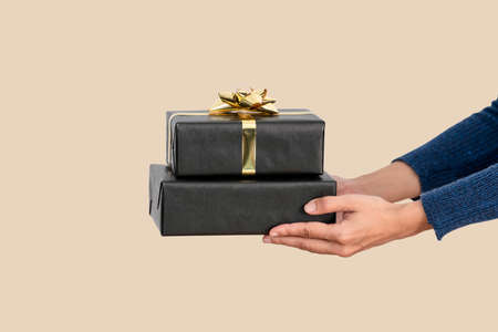 Hand holding black gift box on flesh color background.の写真素材