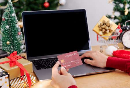 Happy woman holding credit card doing online shopping present at Christmas. Mockup laptop computer with white screen.の写真素材