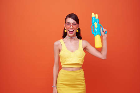 Young woman happy beauty with water gun and during Songkran festival studio shot isolated on orange background.の写真素材