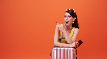happy woman girl with suitcase and passport pointing her finger on orange background. concept of...
