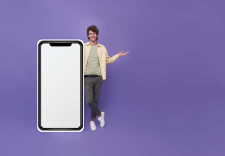 Young handsome man standing with mockup big Smartphone blank white screen isolated on purple studio background.の写真素材